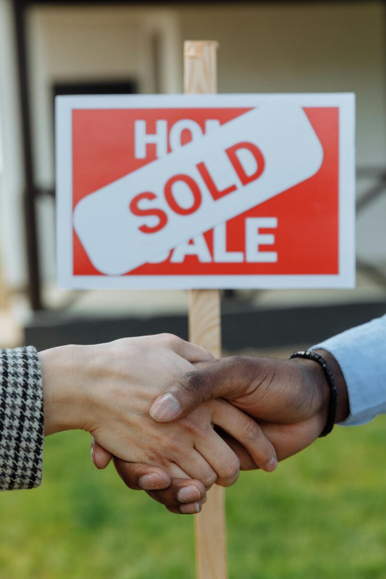 Close-up of a handshake in front of a sold sign symbolizing a successful real estate transaction.